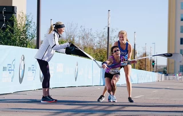 Coureuse épuisée soutenue par une autre à l’arrivée d’un marathon, métaphore du burn-out et du leadership au travail